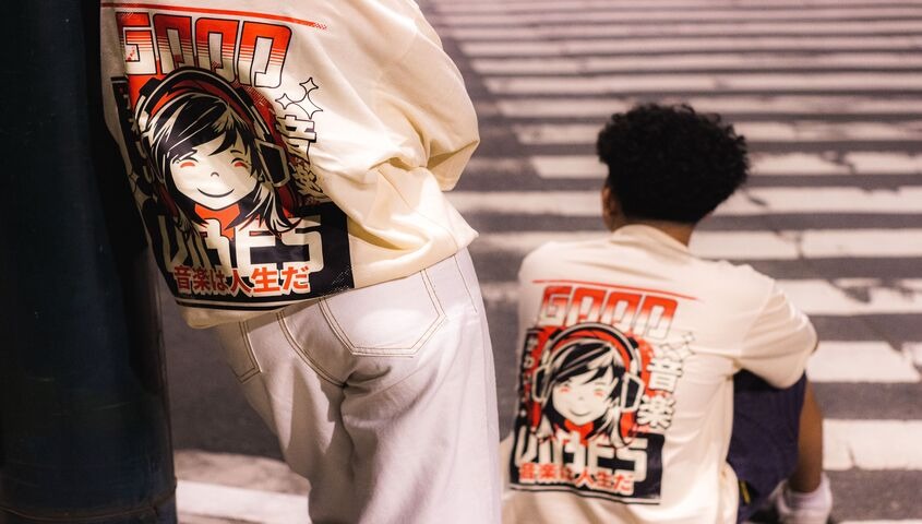 Two people wearing matching cream streetwear T-shirts with a red anime graphic print