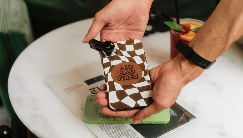 Hands holding a checkerboard phone case with a No Bad Vibes graphic