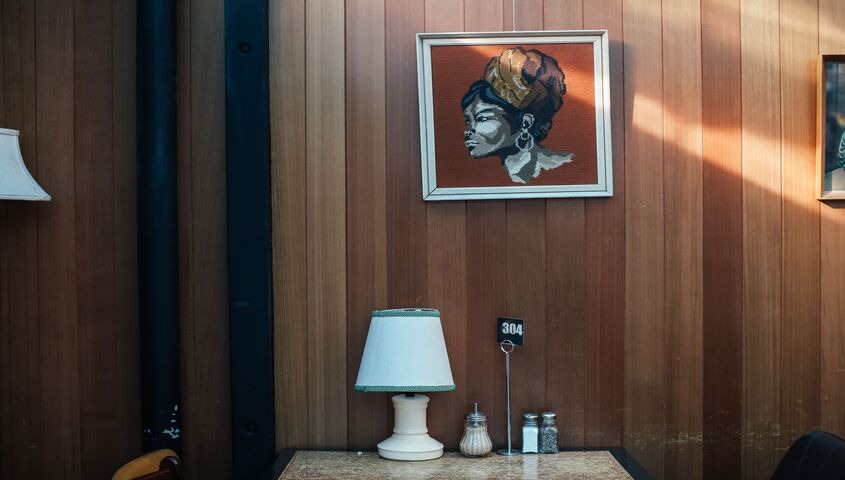 Framed portrait artwork hanging on a wood-panelled wall above a table lamp