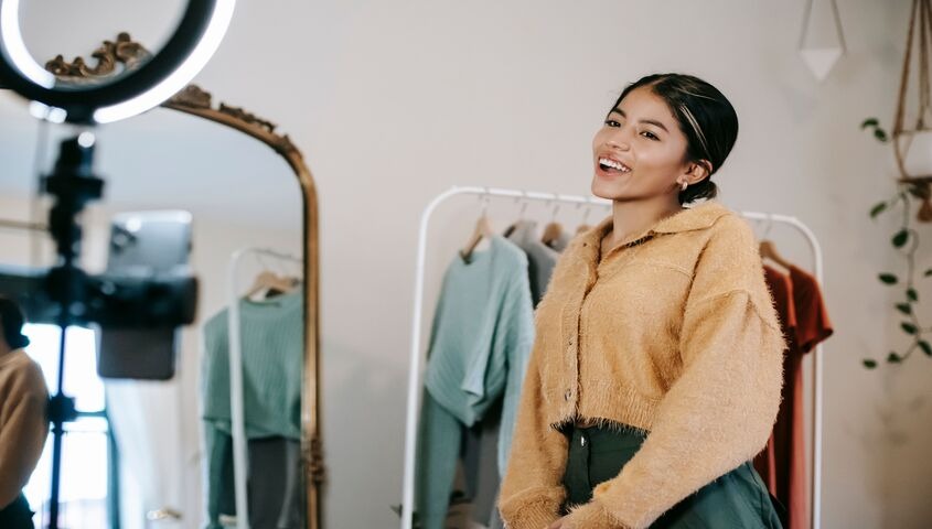 Creator smiling beside a clothing rack and ring light, running the setup steps of how to sell on tiktok shop for beginners.