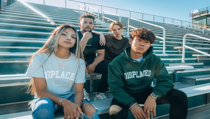 Four friends wearing matching branded tees and hoodies on stadium bleachers, a branded dropshipping line out in the wild.