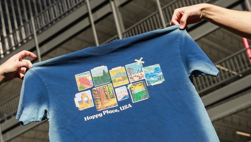 Hands holding up a printed blue T-shirt to check the graphic's size and position