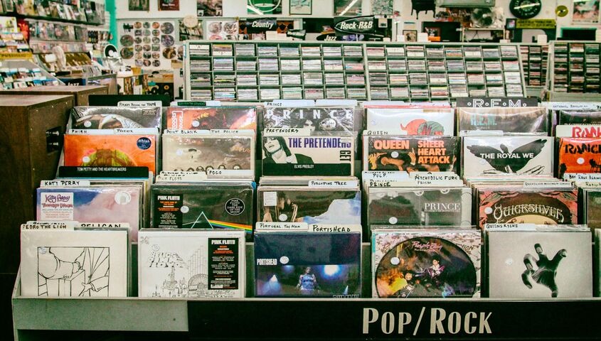 Rows of vinyl records in a shop's pop/rock section, the physical-sales world where custom band merch still earns.