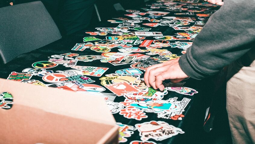 Hand picking through a table covered in stickers, one of the cheapest band merch ideas that keeps working long after the show.