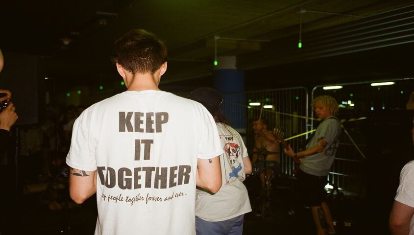 Fan in a bold text tee watching a band from the barrier, showing the design rule behind good custom band merch.