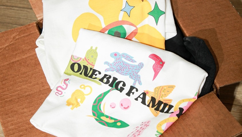 Folded white T-shirts with colorful custom prints packed in a cardboard shipping box