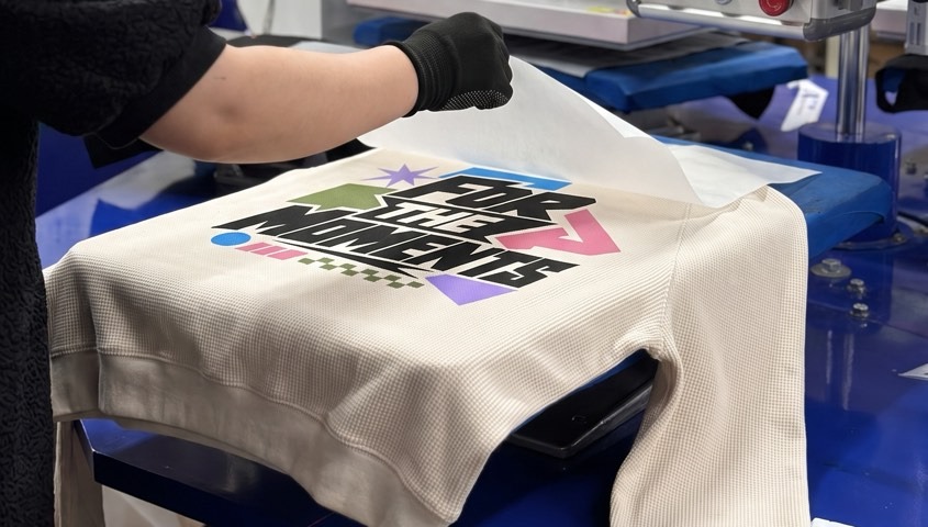 Production worker peeling transfer film from a printed graphic on a cream sweatshirt
