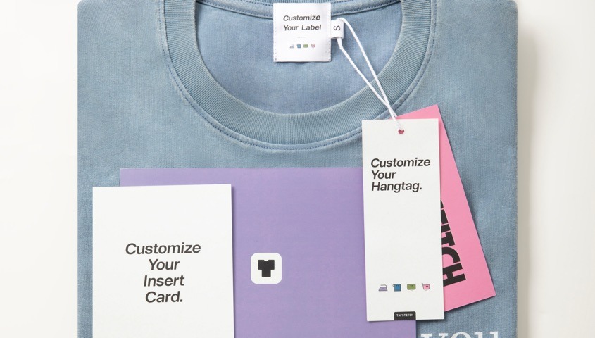 Folded blue sweatshirt with a custom neck label, hangtag and insert card