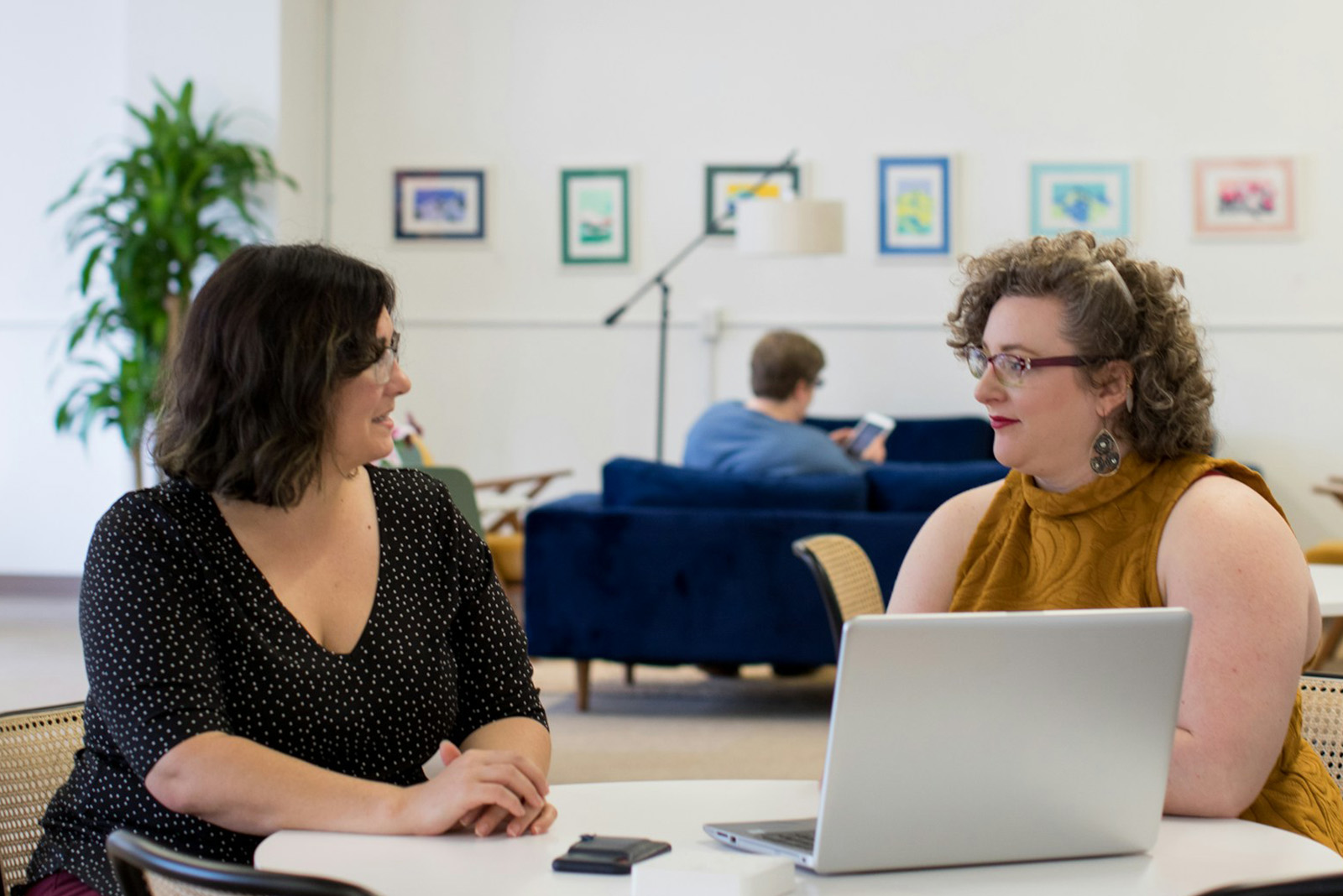 Zwei Frauen sitzen an einem Tisch und unterhalten sich vor einem Laptop.