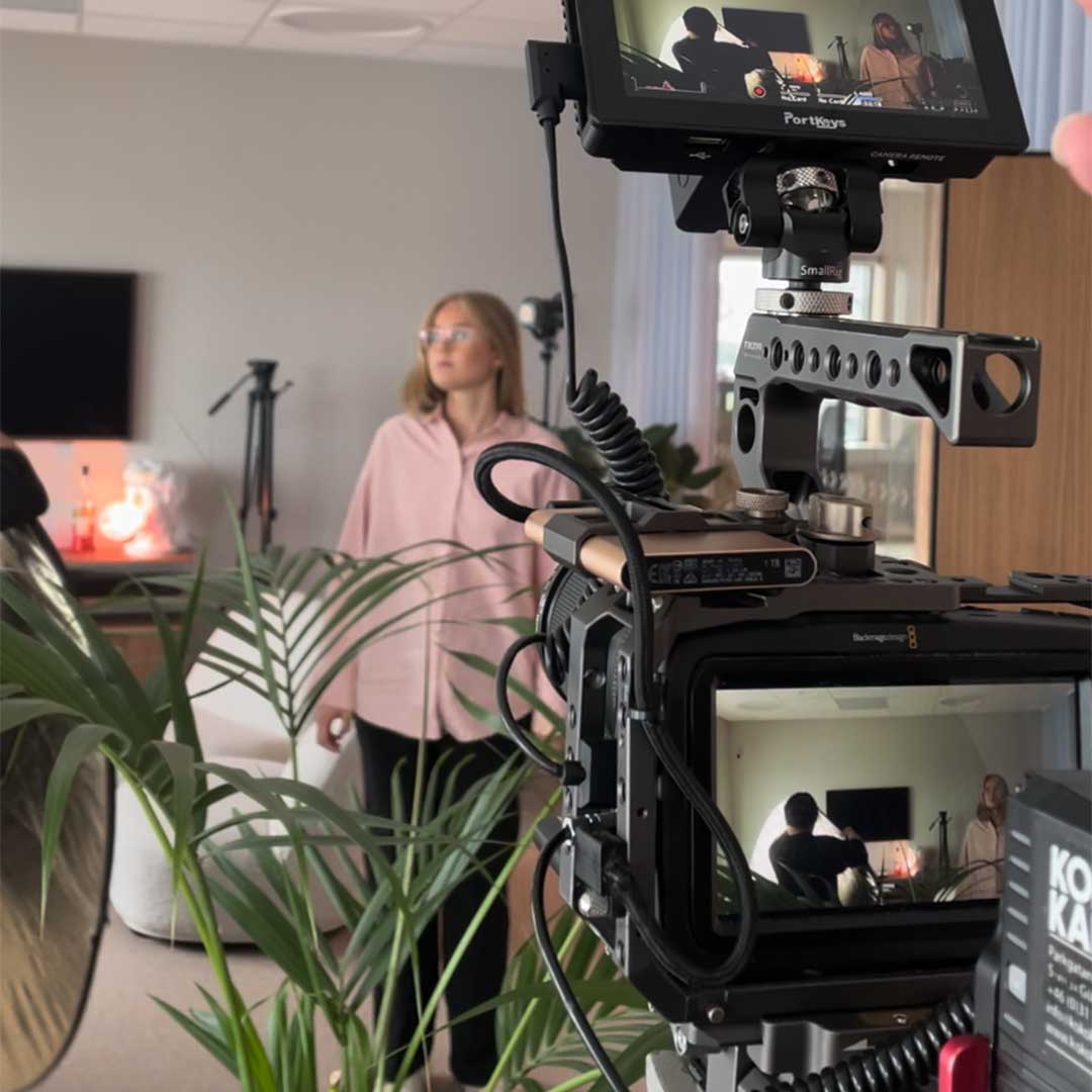 Kvinna i rosa skjorta filmad med professionell kamera i ett rum med växter.