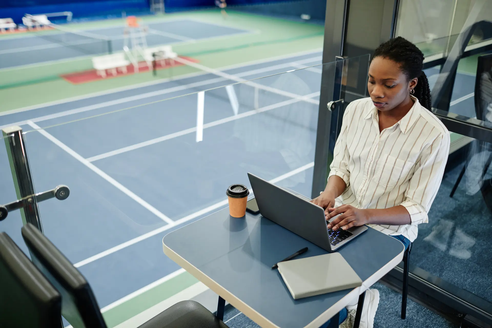 Athletics communications staffer works on a laptop overlooking a tennis court, the daily use case for sports information director software