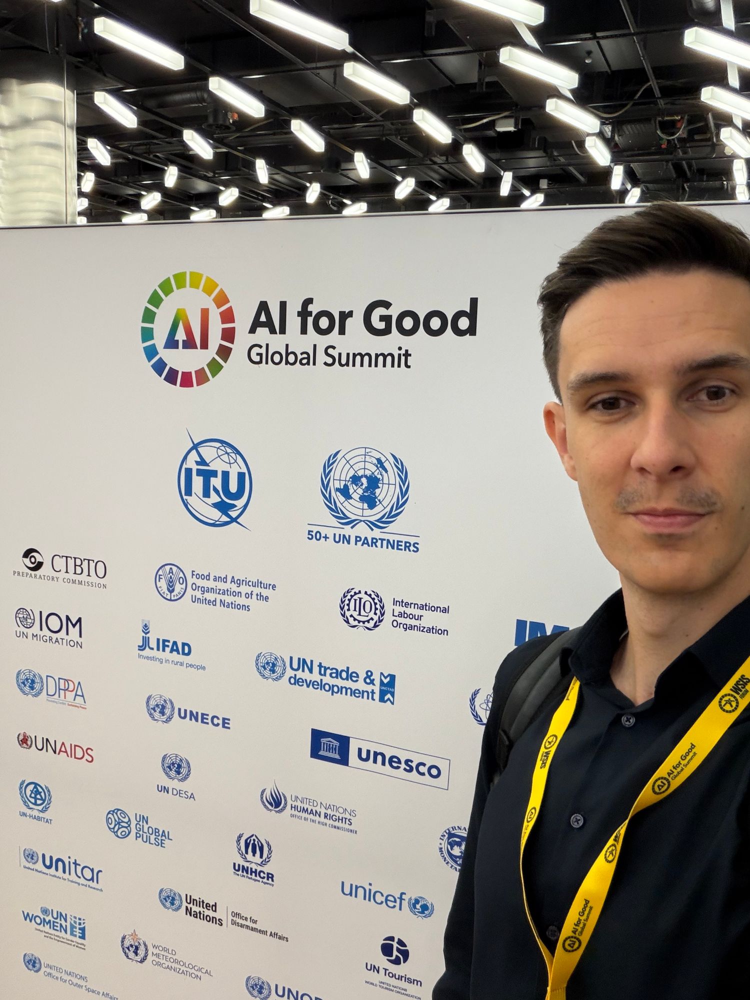 Selfie in front of the AI for Good Global Summit partner wall with ITU, UNESCO, UNICEF and other UN logos