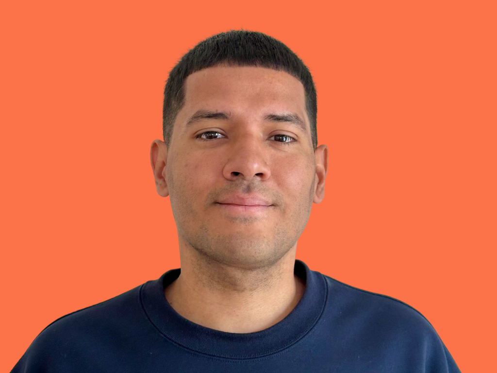 Portrait of Juan Estupinan founder of focuswave wearing a dark blue sweatshirt against an orange background.