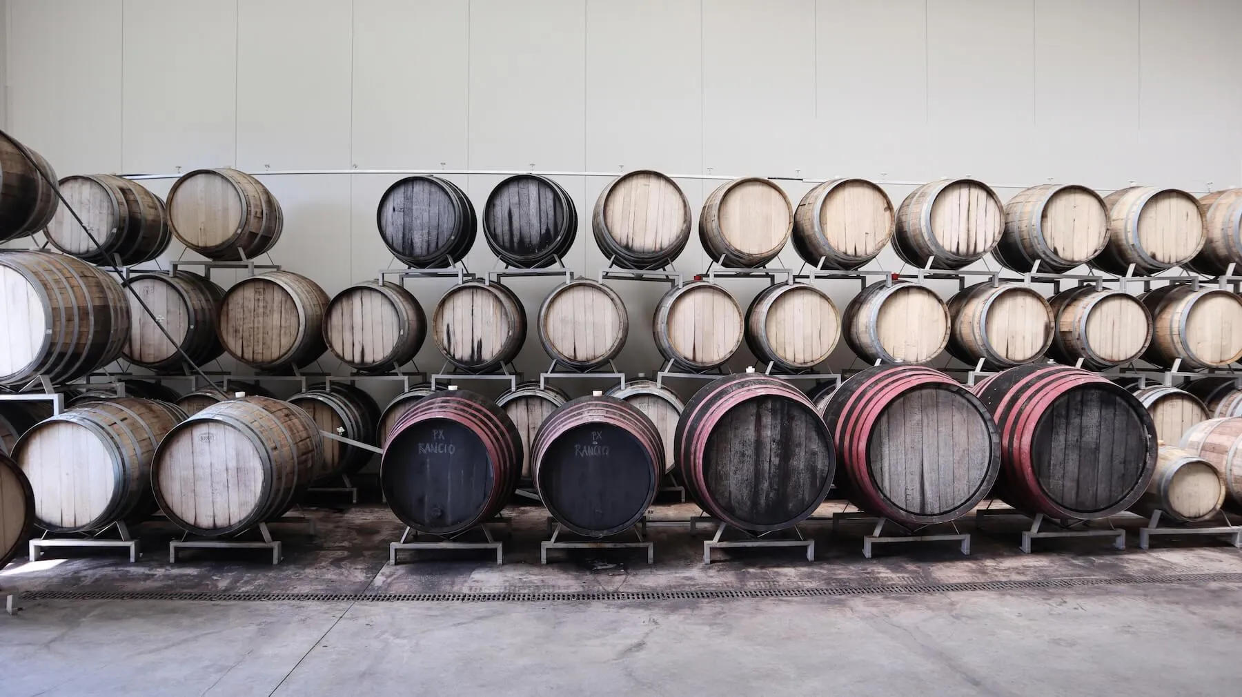 Rows of wooden wine barrels stacked on metal racks inside a winery cellar.