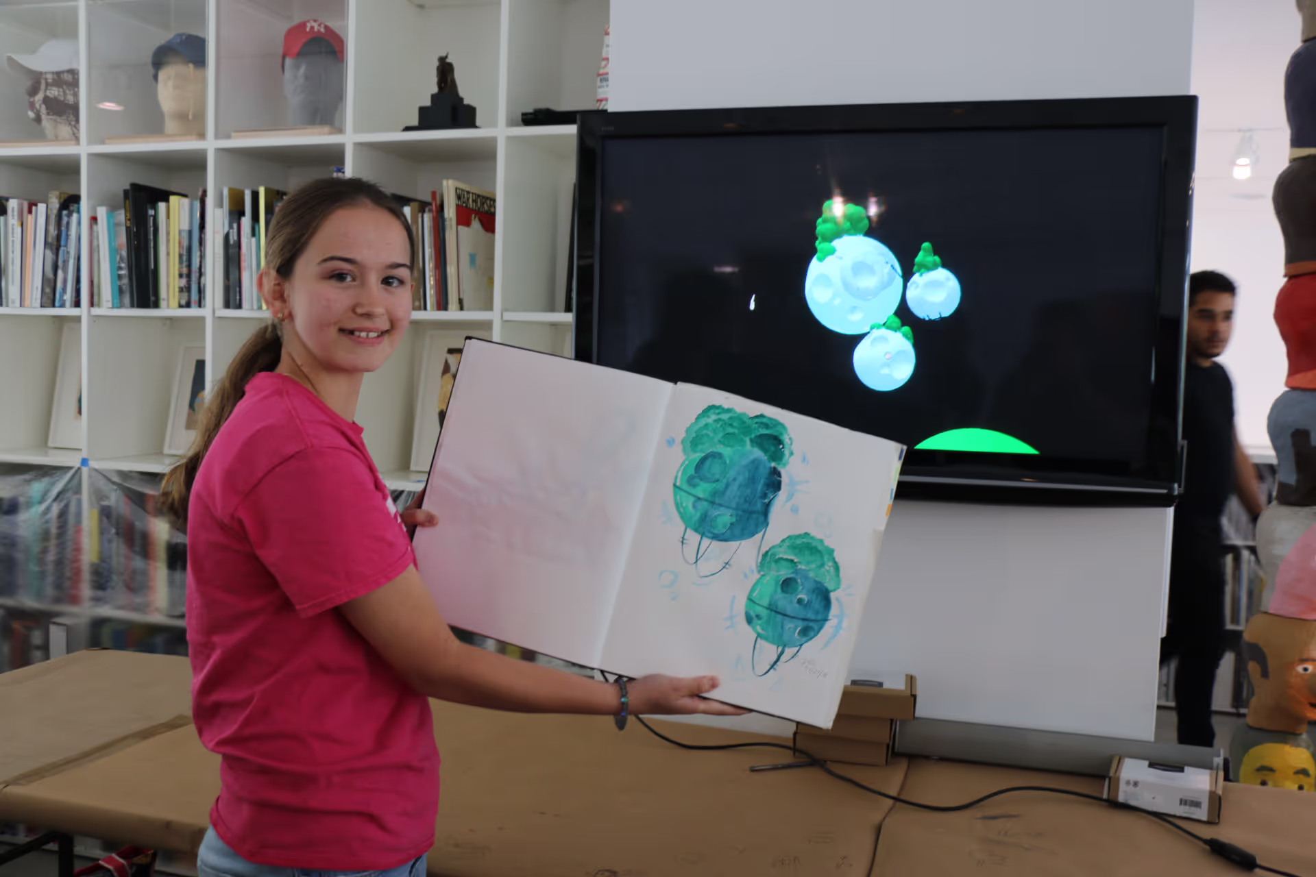 MUD Foundation XRCamp Art at the De La Cruz Collection in Miami, Florida, 2018, featuring a girl holding a sketchbook with blue-green character drawings in an immersive art installation.