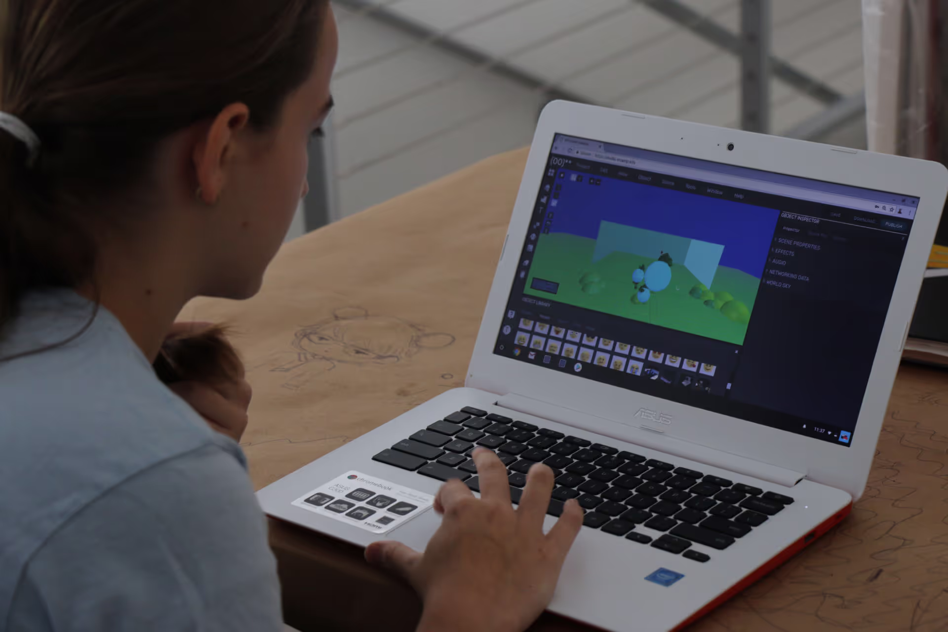 MUD Foundation XRCamp at the De La Cruz Collection in Miami, Florida, 2018, featuring a person working on a white laptop displaying a 3D modeling or animation interface with a colorful digital scene, seated at a wooden table.