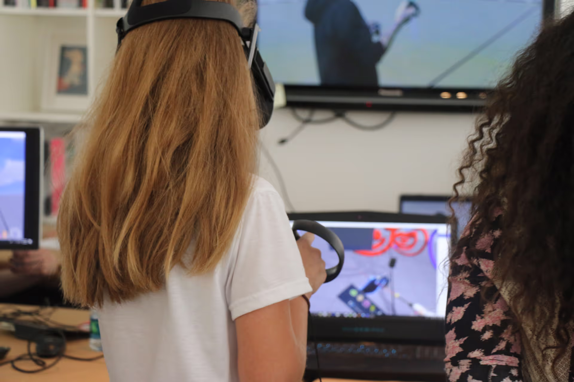 MUD Foundation XRCamp at the De La Cruz Collection in Miami, Florida, 2018, featuring a person wearing a VR headset and holding controllers while facing a laptop displaying a virtual reality interface, with another person and multiple monitors in the room.