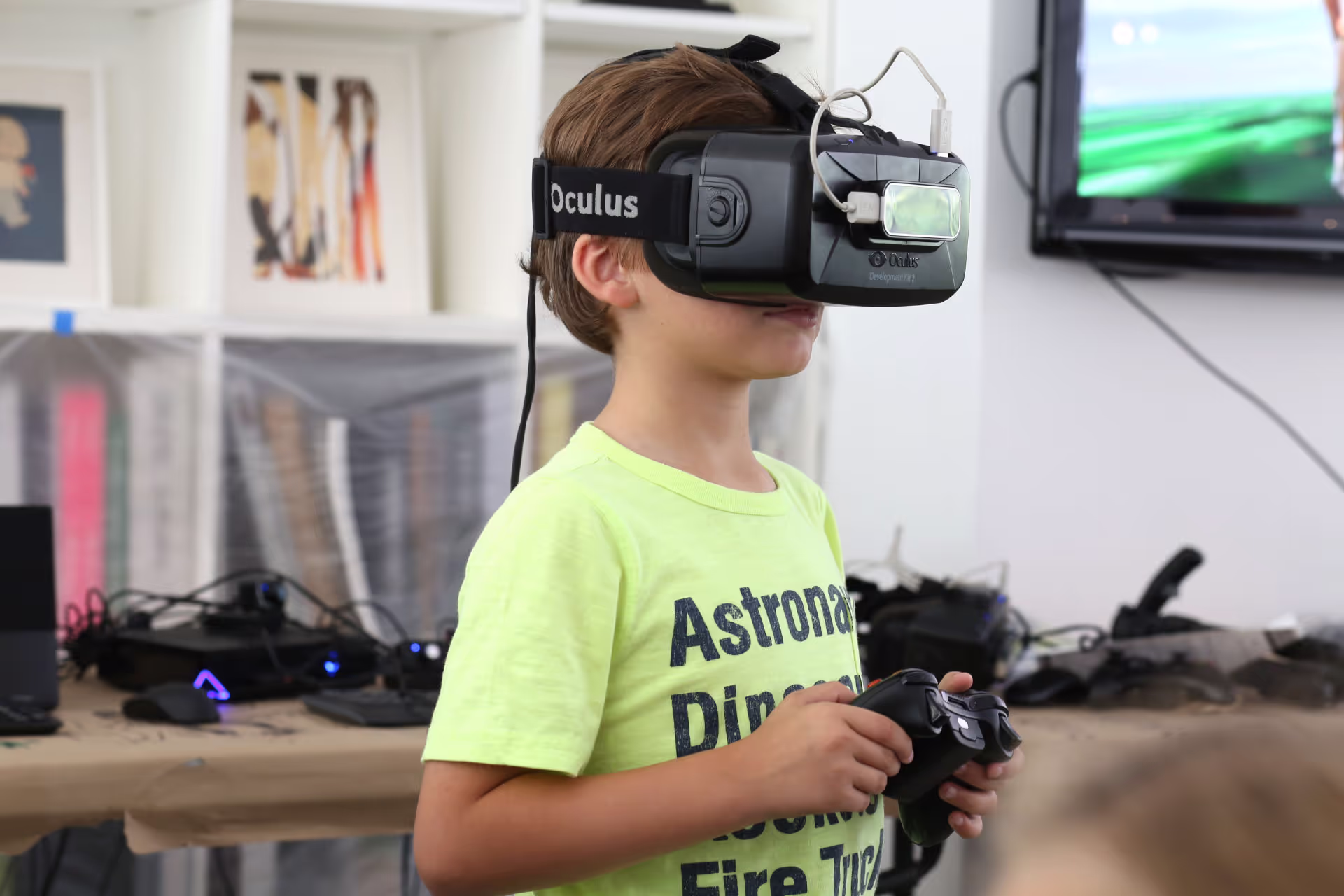 MUD Foundation XRCamp at the De La Cruz Collection in Miami, Florida, 2017, featuring a young boy wearing an Oculus VR headset and holding a game controller, with electronic equipment on tables in the background.