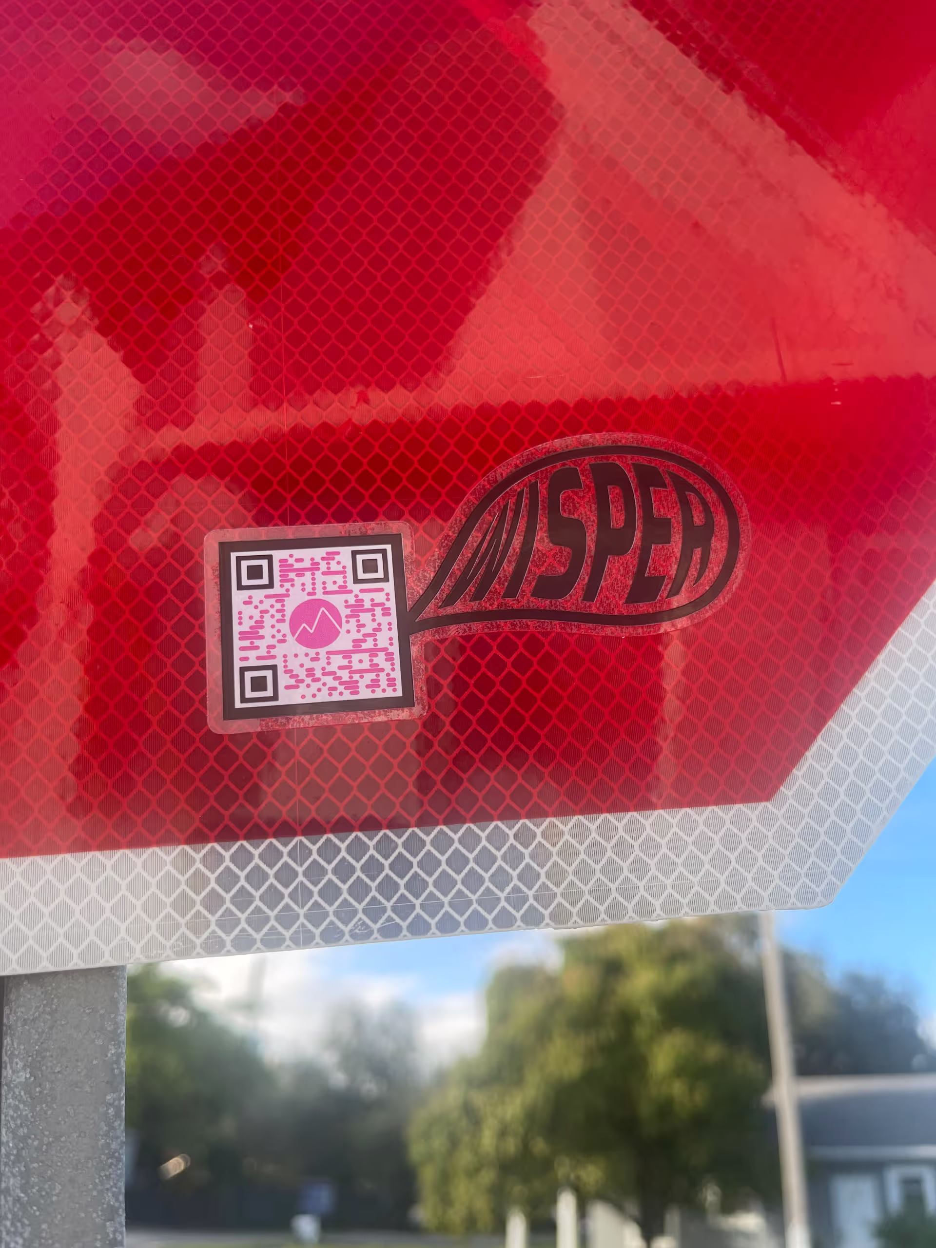 MUD Foundation WISper, featuring a close-up of a red reflective stop sign with a small QR code sticker displaying the word “WISPER” inside a speech bubble.