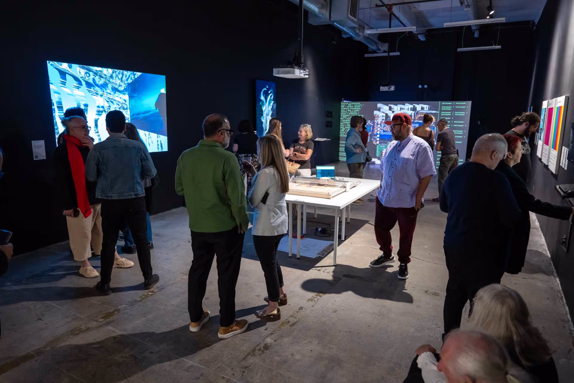 MUD Foundation Media Under Dystopia WISper Edition exhibition 2023, showing visitors viewing digital and physical artworks in a dark gallery with illuminated screens and exhibition tables.