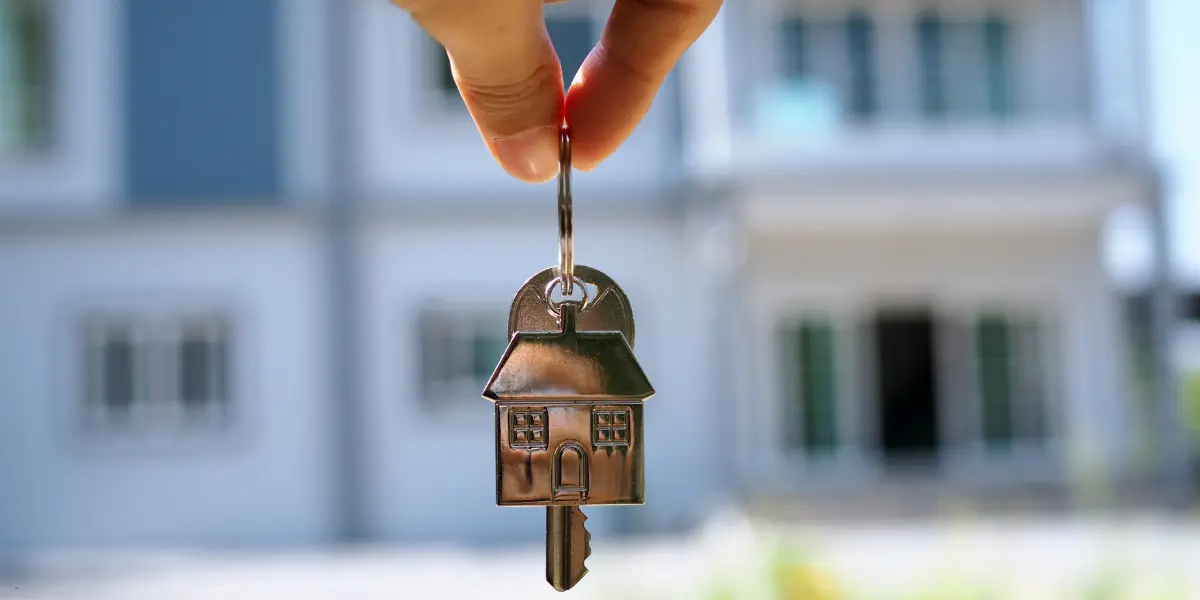 Quick home sale symbolized by a hand holding a house-shaped key in front of a new home