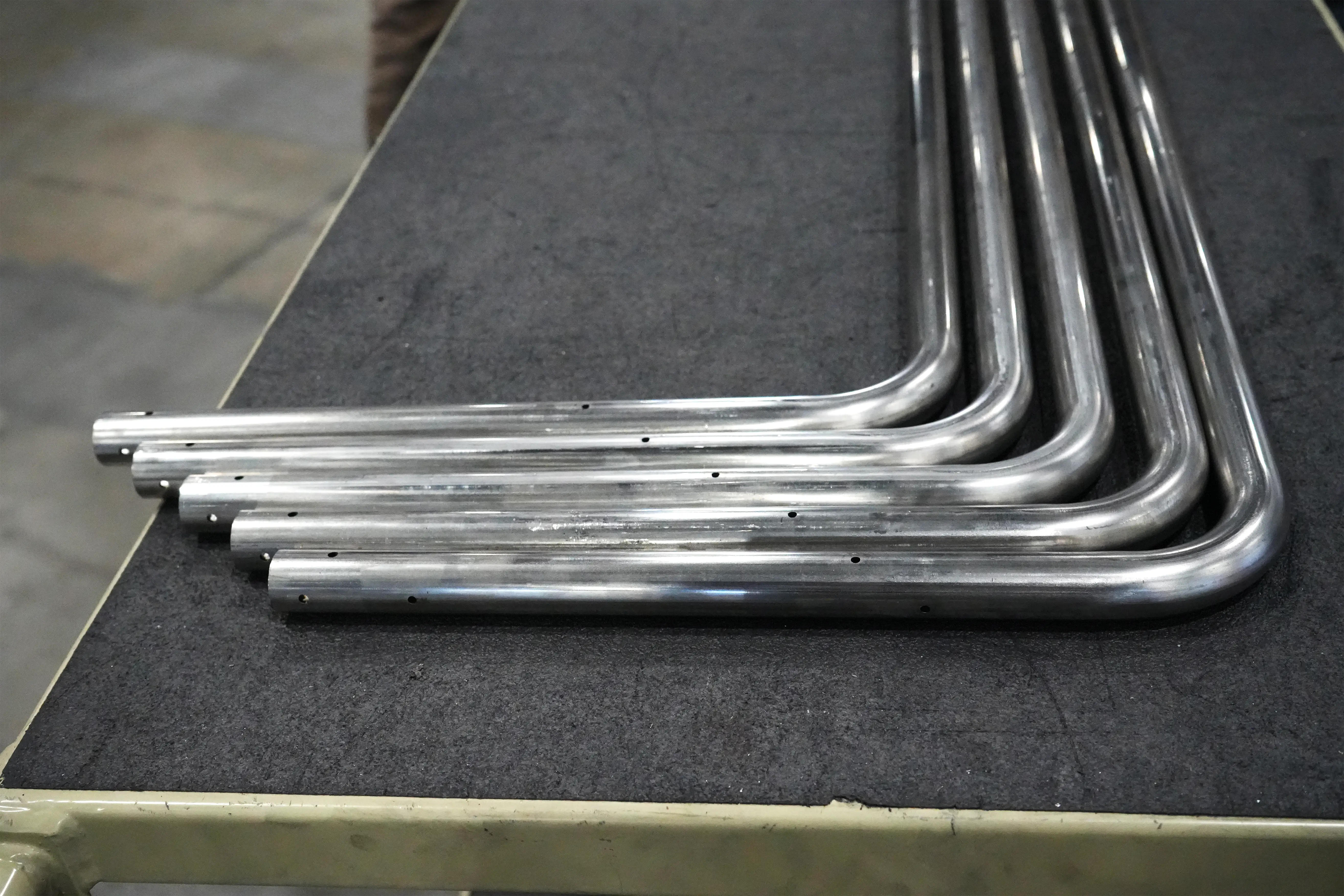 Row of identical bent metal tubes with drilled holes