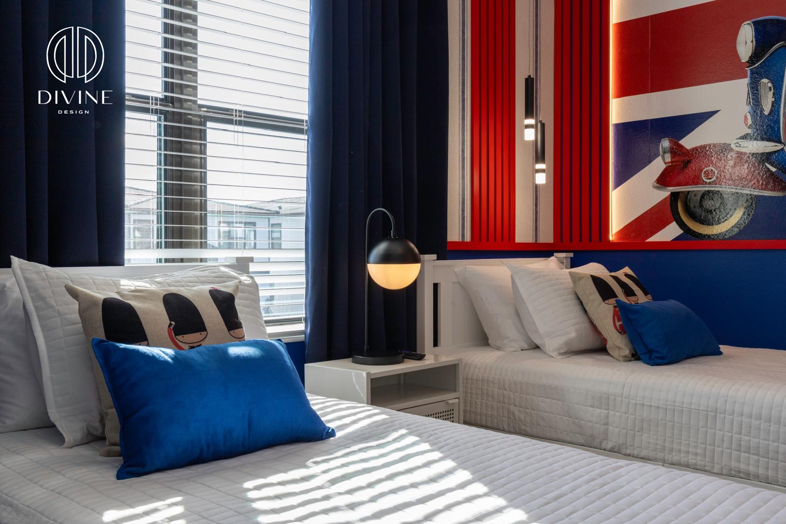 Two single beds with white bedding, colorful pillows, a night lamp, and a Union Jack wall mural.
