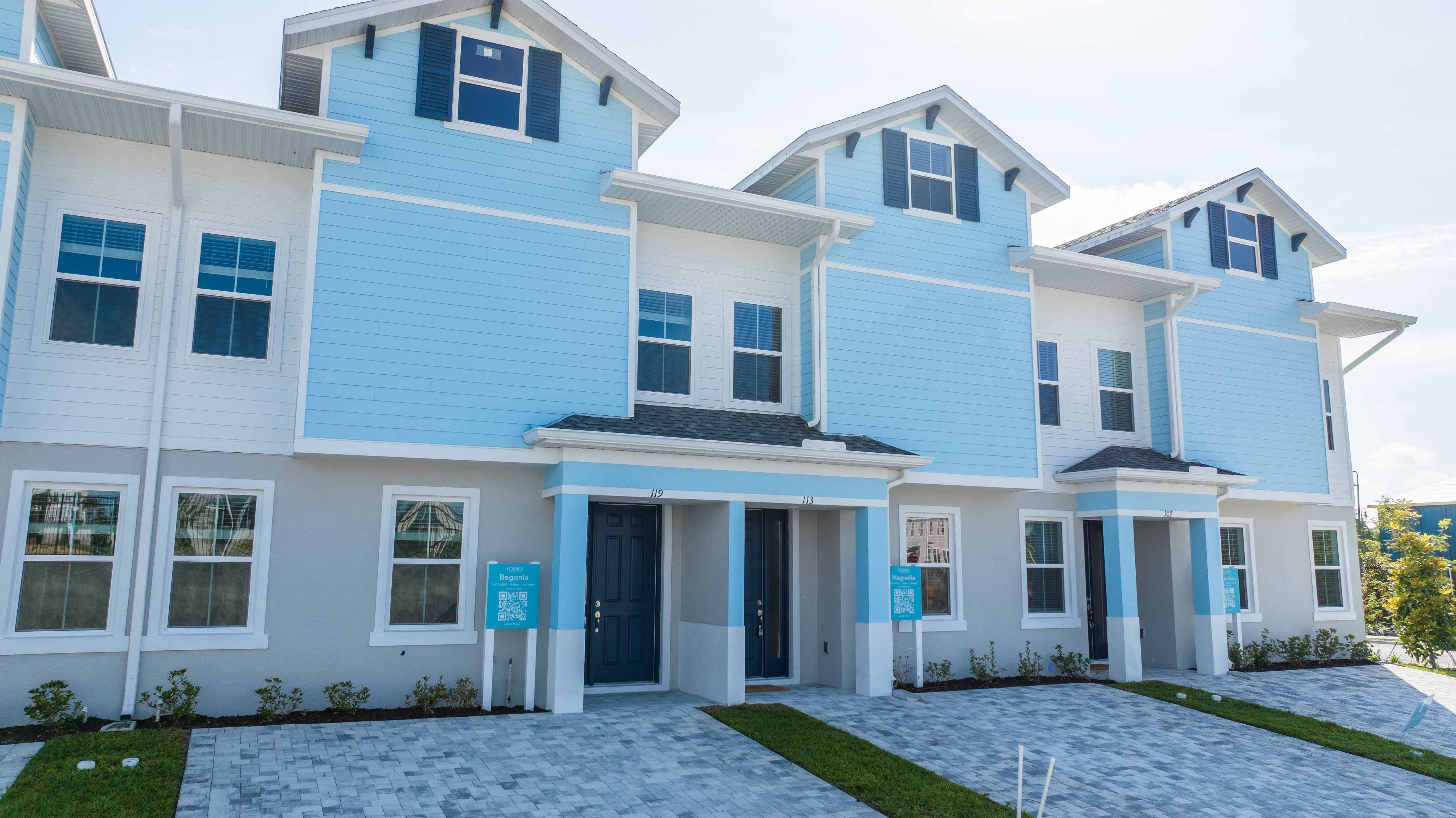 Blue and white modern townhouses with paved driveways and numbered entrances on a sunny day.