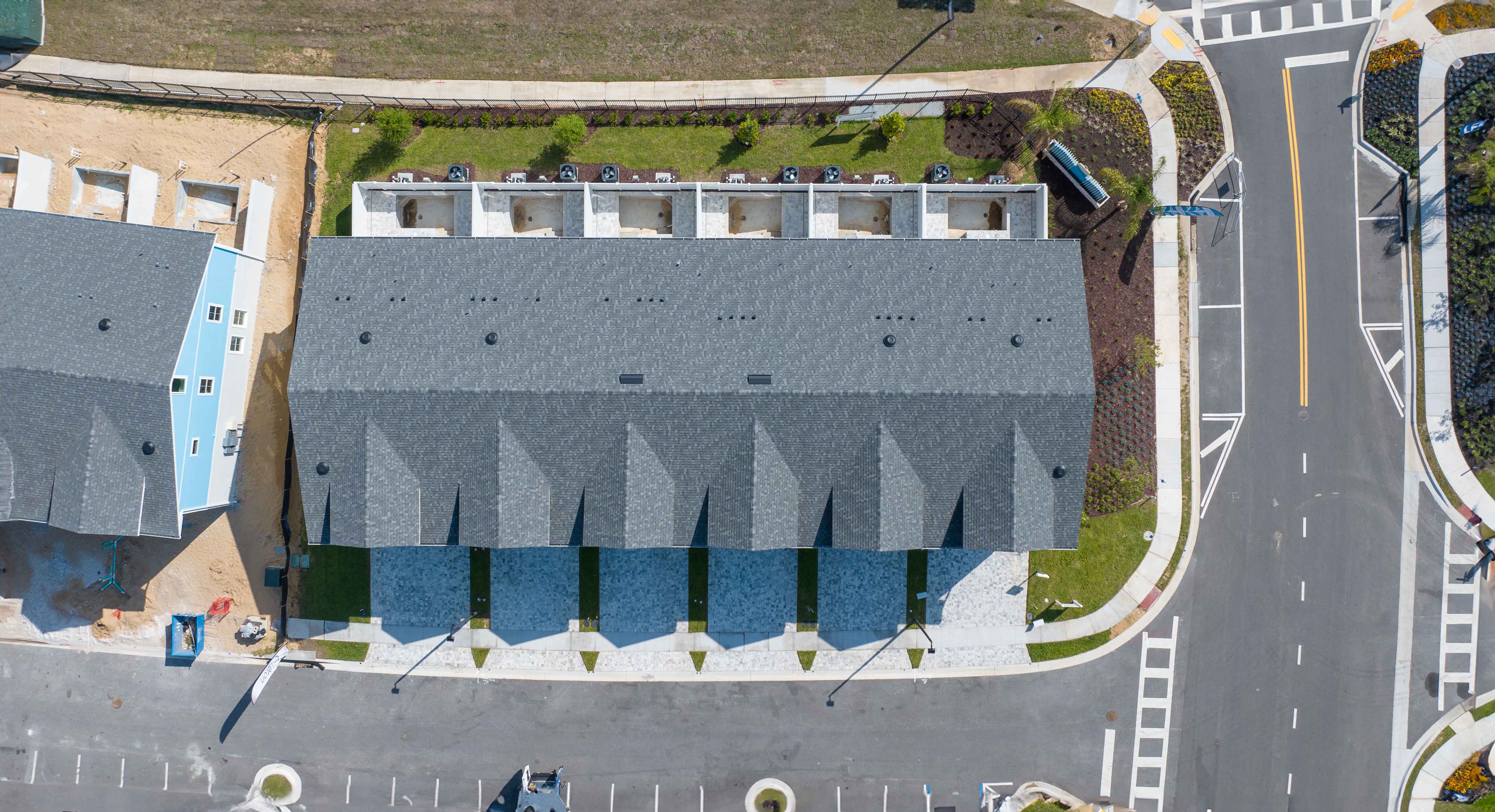 Aerial view of a row of townhouses with gray roofs beside a curved road and parking spaces.