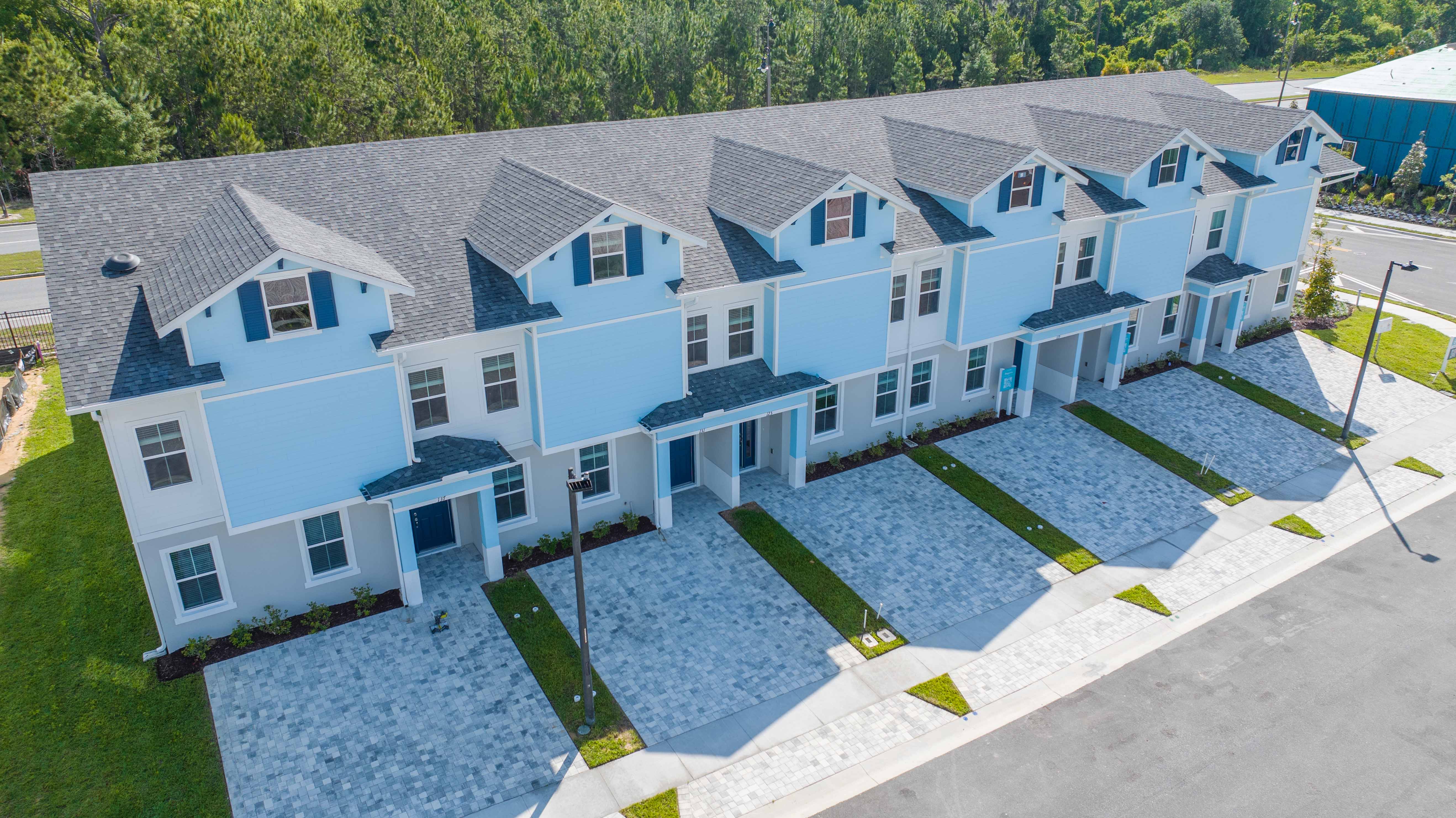 Aerial view of a row of new blue and white townhouses with paved driveways and green lawns.