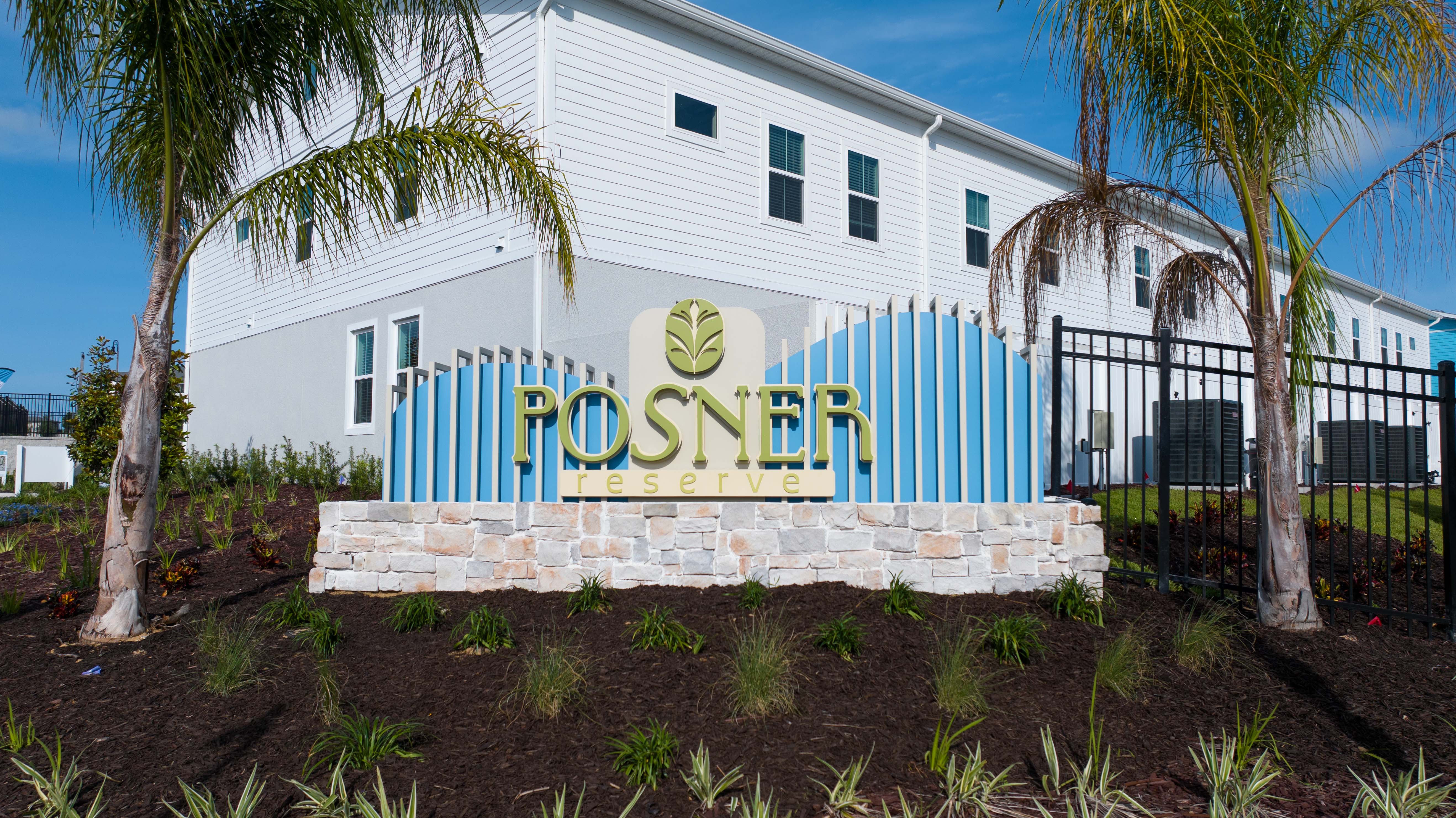 Entrance sign for Posner Reserve with landscaping and a white residential building behind it.