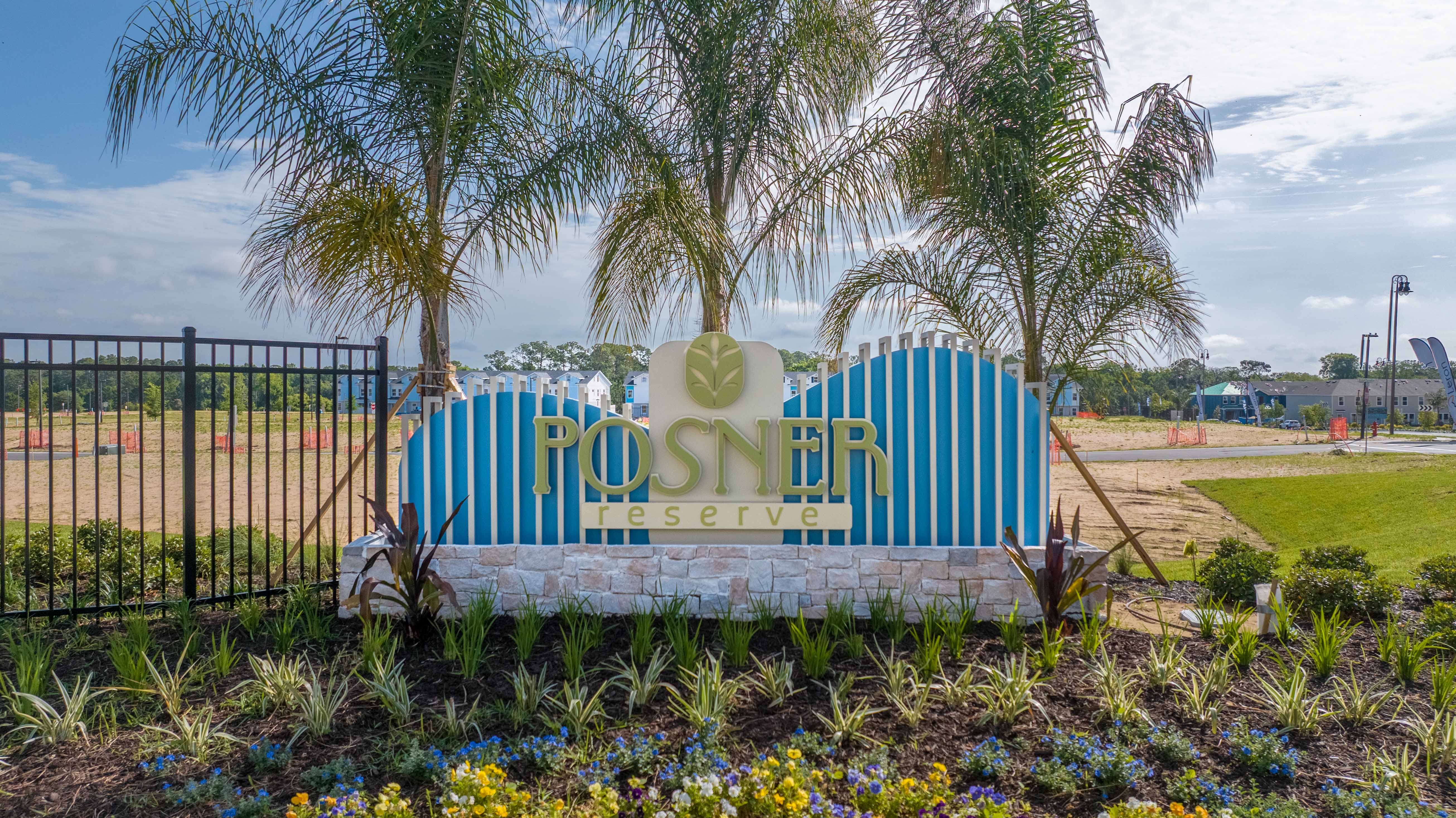 Sign reading 'Posner Reserve' with palm trees and landscaped flowers at a residential development entrance.