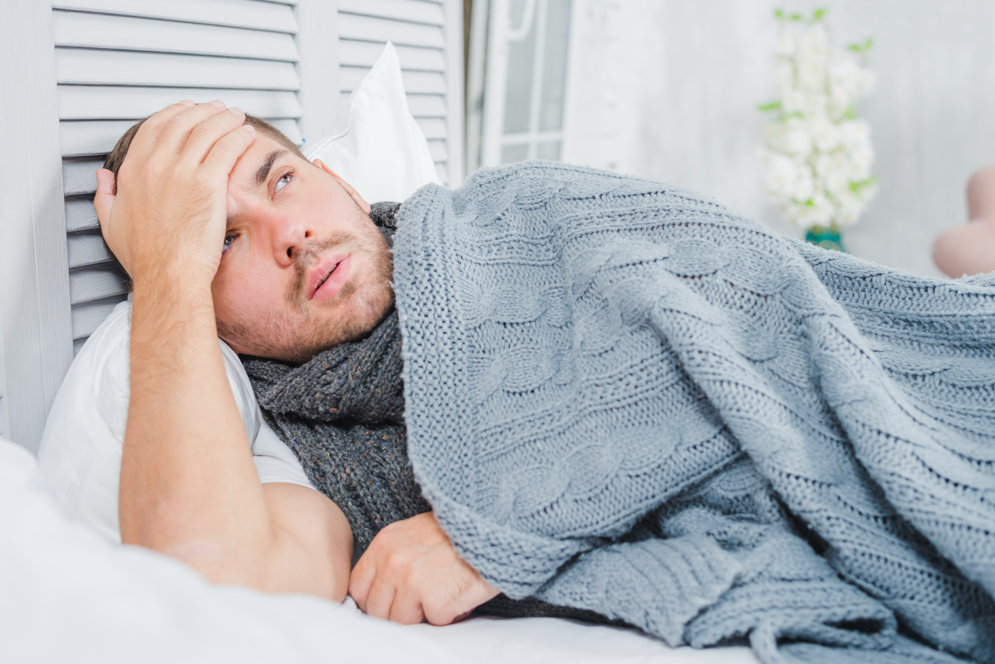 Man experiencing alcohol withdrawal symptoms while resting in bed under a blanket during early recovery