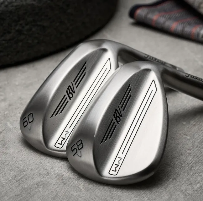 Close-up of two silver golf wedges with BV and SM markings, numbered 58 and 60, resting on a gray surface.