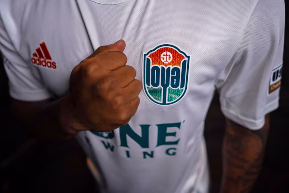 Close-up of a person wearing a white jersey with a clenched fist over the chest and a '50 loyal' badge on the left side.