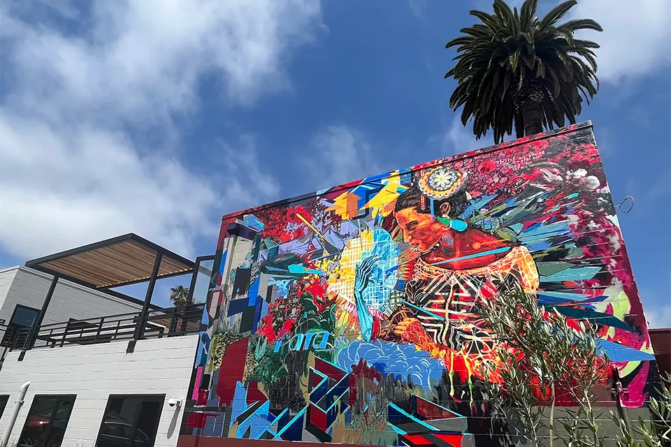 Colorful mural on a building wall depicting a woman in traditional attire surrounded by vibrant abstract patterns and shapes.