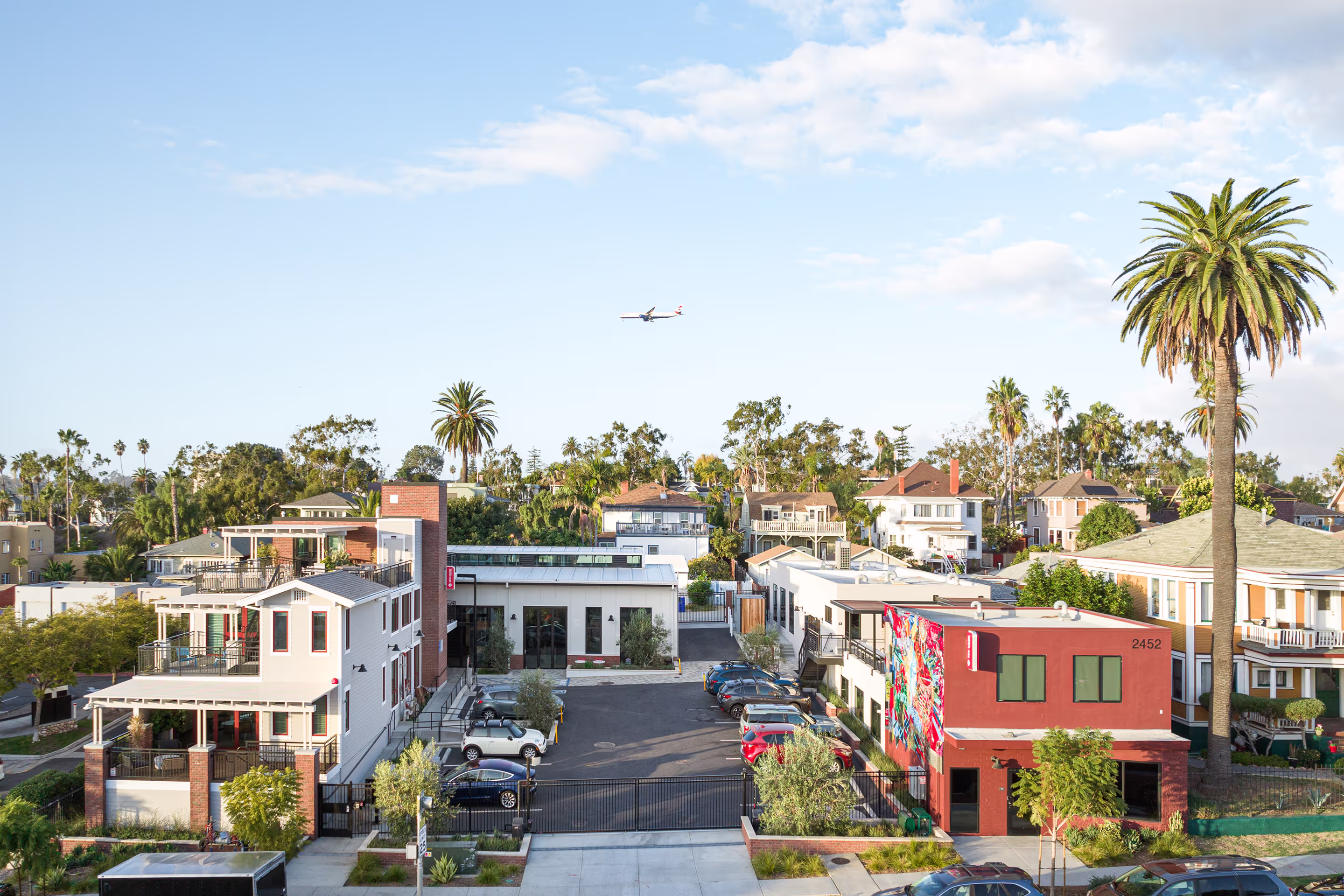 Red Door Interactive Headquarters building with a colorful mural, parking lot, palm trees, and an airplane flying overhead under a clear sky.