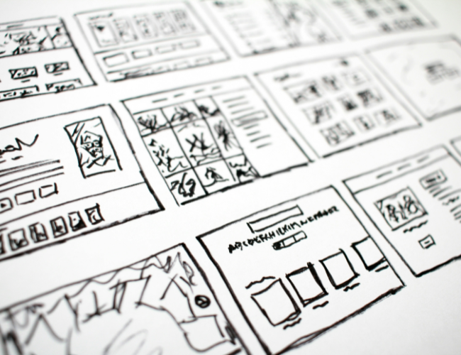 Hand-drawn website wireframe sketches and storyboards spread across a desk in black ink on white paper.