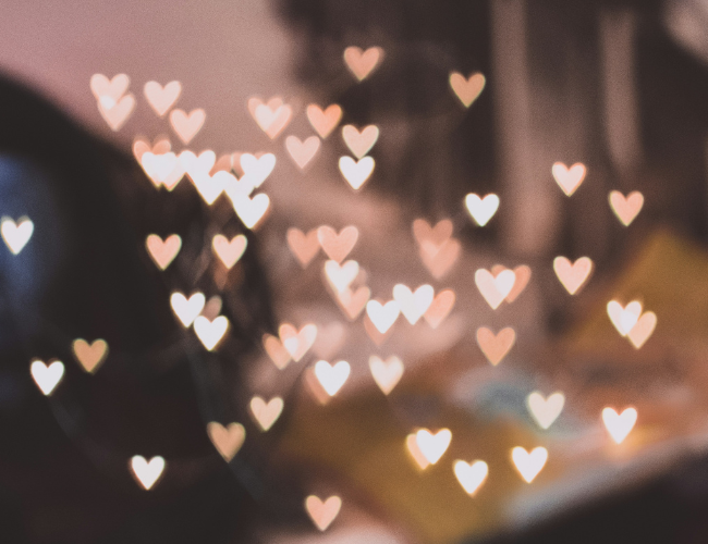 Soft-focus heart-shaped bokeh lights scattered against a dark warm-toned background.