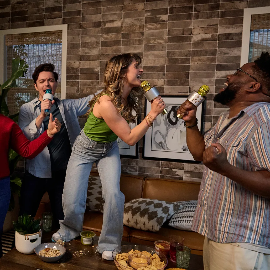 A lively karaoke party with friends singing and dancing on a couch, surrounded by snacks and drinks in a cozy living room.