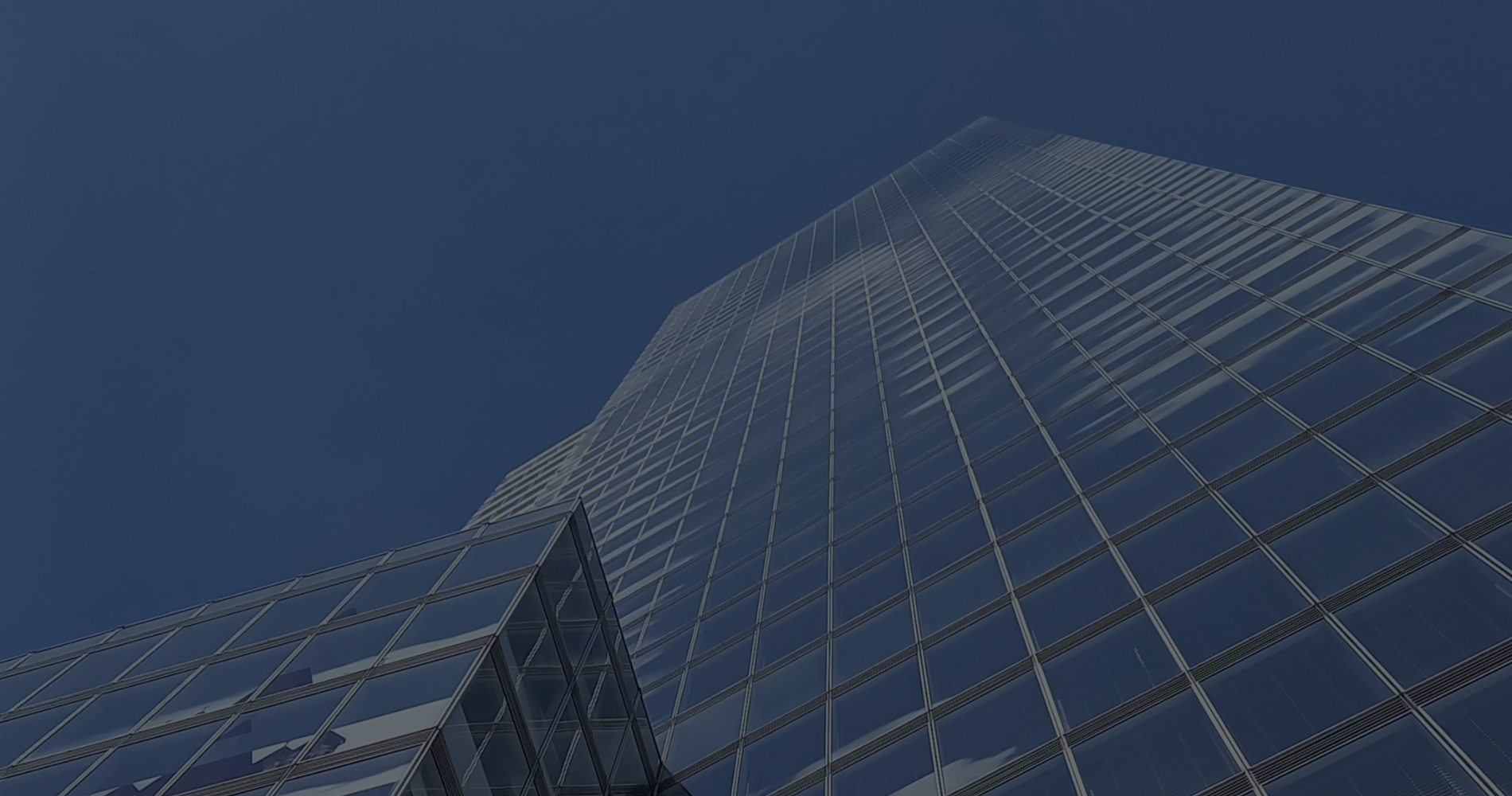 Low-angle view of a tall glass office tower reflecting a clear blue sky.
