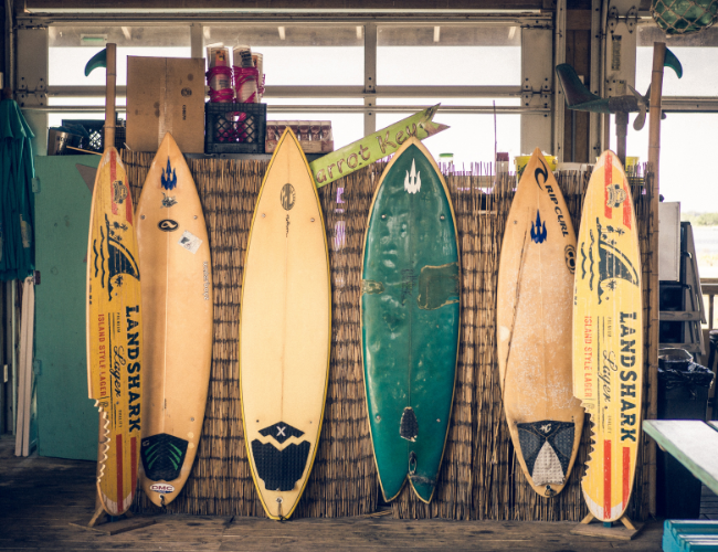 Five surfboards lined up vertically against a wooden garage wall.