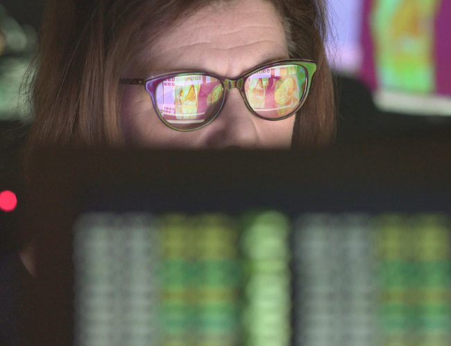 Close-up of a woman's eyes behind glasses reflecting colorful medical or scientific imaging data displayed on a computer monitor.