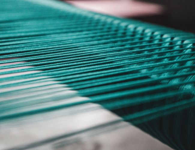 Close-up of bright teal threads stretched parallel on a weaving loom.