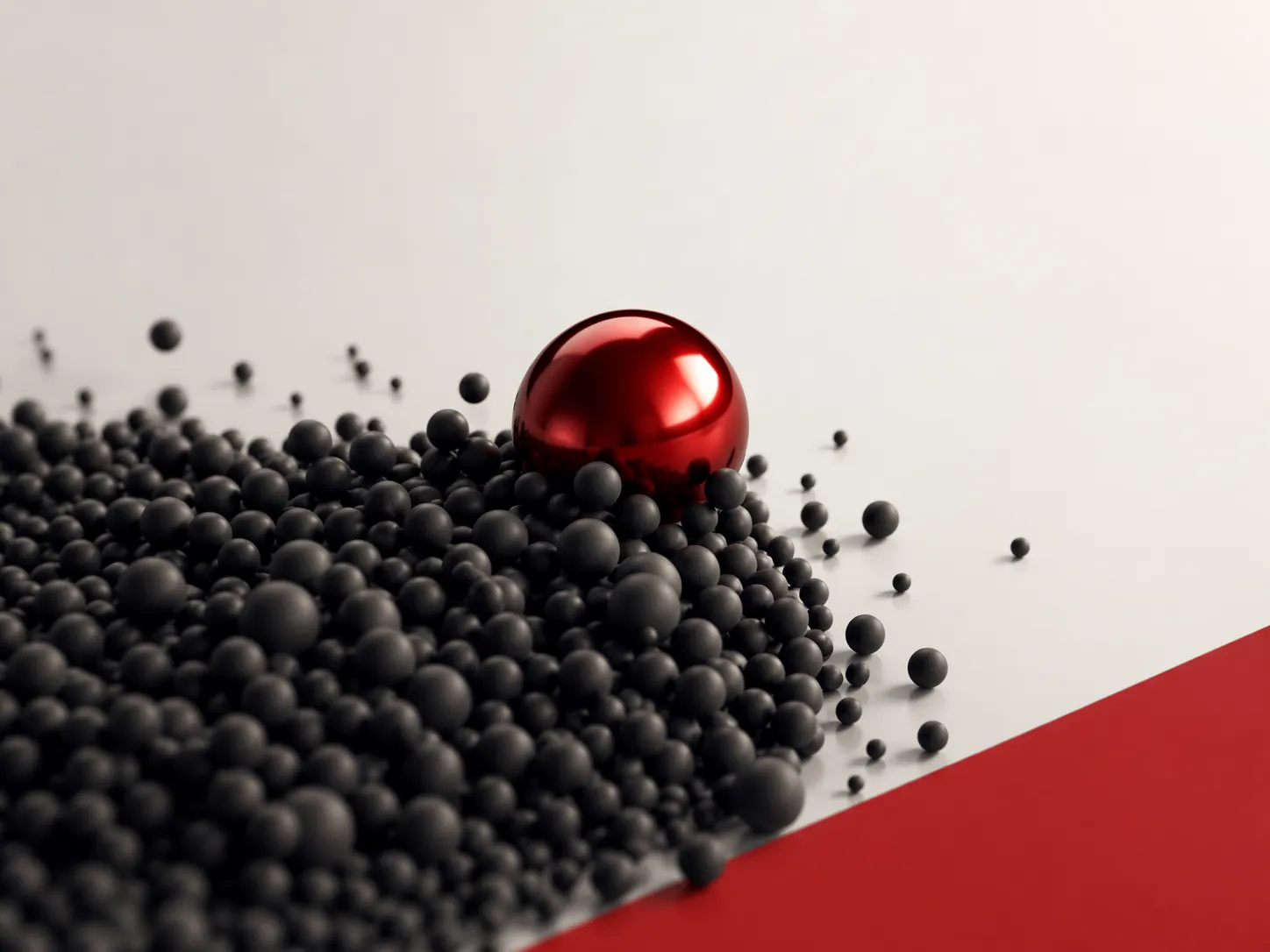 A glossy red sphere emerging from a cluster of matte black particles on a clean, minimalist background.