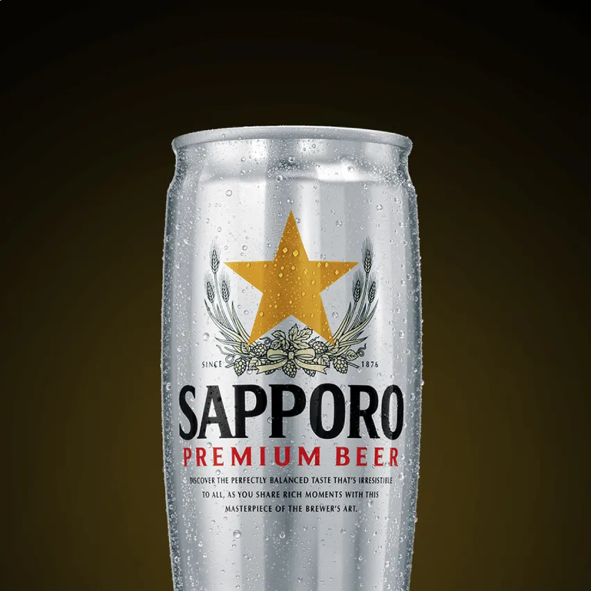 Tall silver can of Sapporo Premium Beer, adorned with a gold star and barley motifs. The can glistens with condensation, set against a dark background.