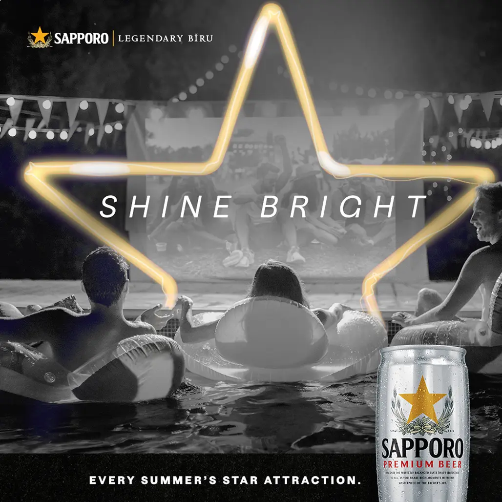 People on pool floats enjoy a movie under string lights. A glowing star frames "Shine Bright." Sapporo beer can in the foreground. Cozy, festive vibe.