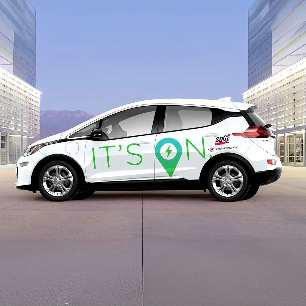 A white electric vehicle wrapped with the SDG&E "It's ON." campaign logo and branding, parked in front of a modern building.