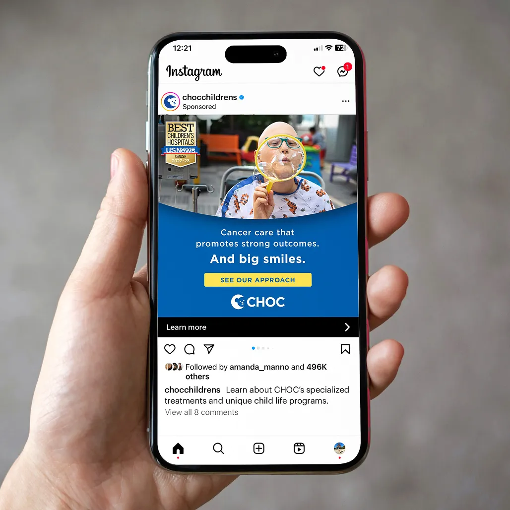 A hand holding a smartphone displaying an Instagram post from CHOC Children's Hospital. It shows a child with cancer blowing bubbles and smiling, accompanied by text promoting cancer care and support. The tone is uplifting and positive.