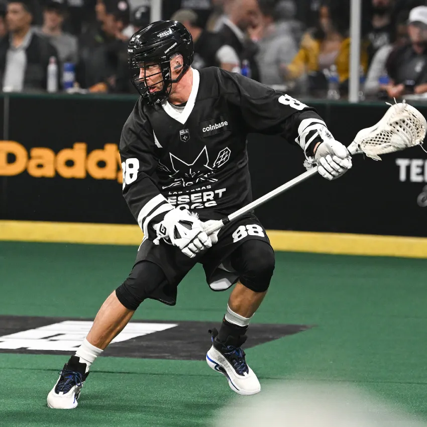 Desert Dogs player #88 in black uniform cuts across the turf with his lacrosse stick extended during an indoor NLL game.